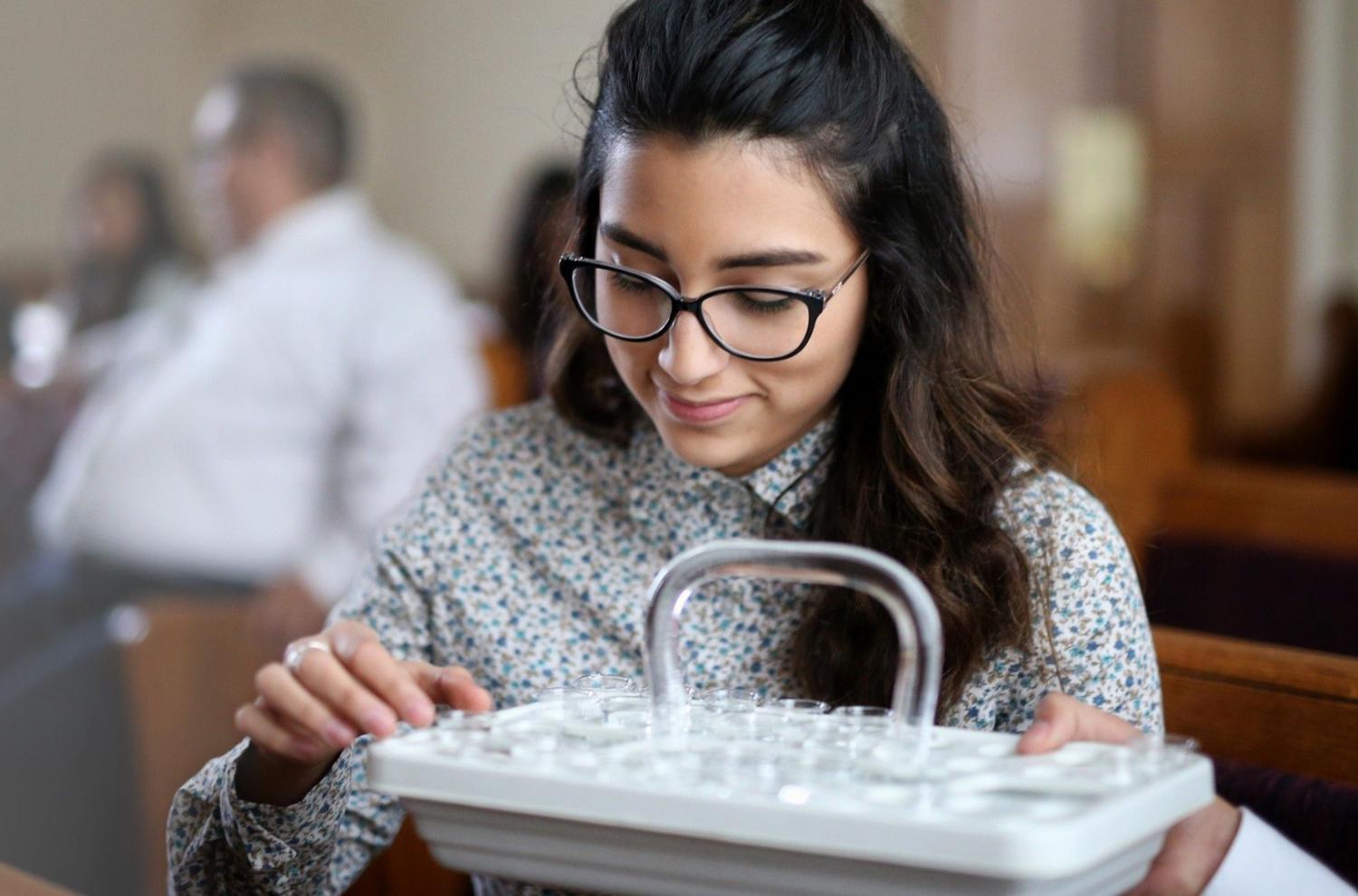 A young woman takes a cup of water from the tray during the Sacrament ordinance. Image courtesy of The Church of Jesus Christ of Latter-day Saints.